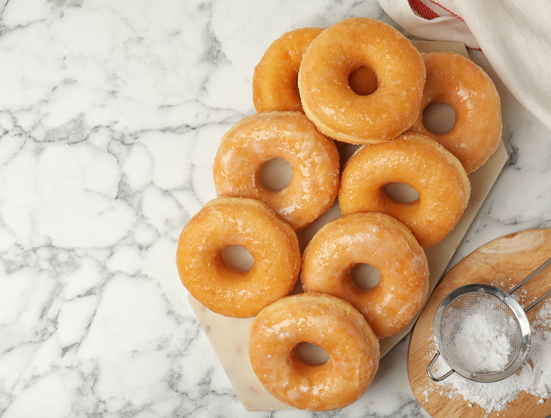 Un plateau de donuts fraîchement frits, dorés et recouverts de glaçage sucré, posé sur une table de cuisine rustique en bois.