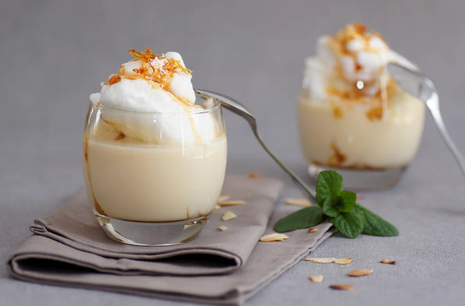 Une carafe en verre débordante de crème anglaise onctueuse, avec une gousse de vanille et des grains de vanille flottant à la surface.